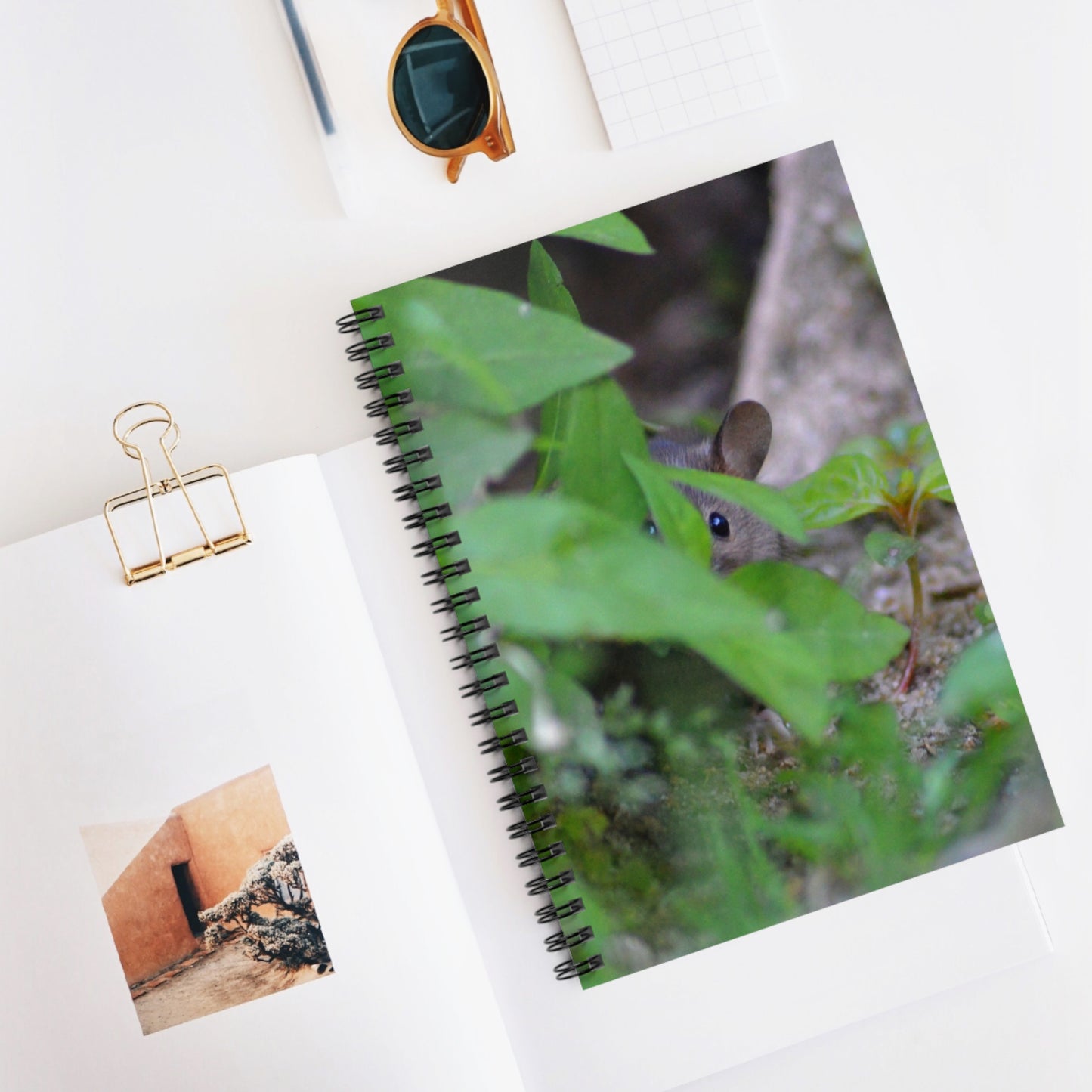 Notebook with a nature-themed cover featuring a mouse among leaves, on a white surface with a clip and small photo.