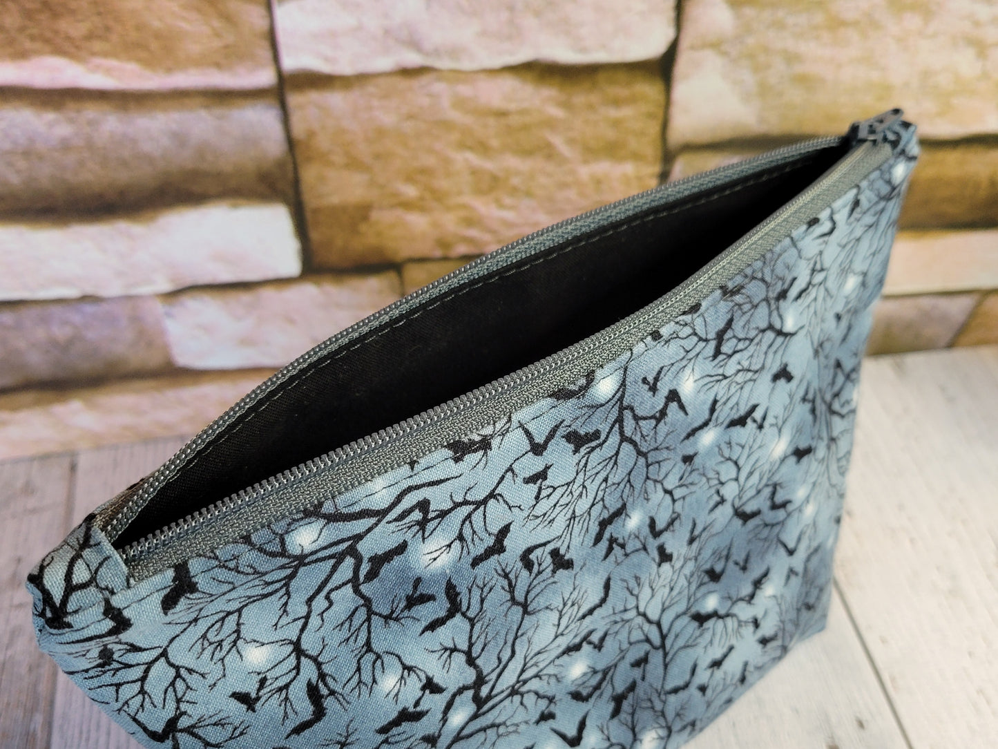 Blue/Gray pouch with black tree pattern and small bats and gray zipper on a wooden surface.