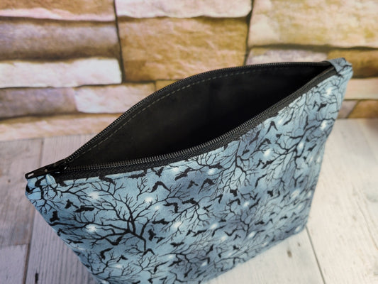 Blue/Gray pouch with black tree pattern and small bats with a solid black lining on a wooden surface.